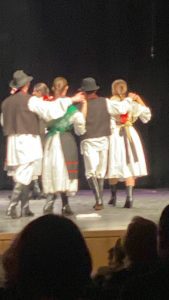 Three dancing couples seen from behind, arms linked, in Slavonian-style costumes.