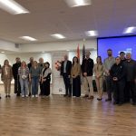 About twenty adults stand together in a parish hall beside the Hrvatska škola Kardinal Stepinac roll-up banner, with the Croatian and American flags behind them.