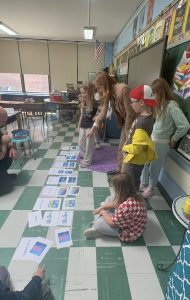 Students gather around Croatian word cards and pictures laid out on the classroom floor during a language game.