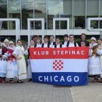 Klub Stepinac dancers in Croatian folk costumes holding the Klub Stepinac Chicago flag in front of the HAMILTON sign at Hamilton City Hall.