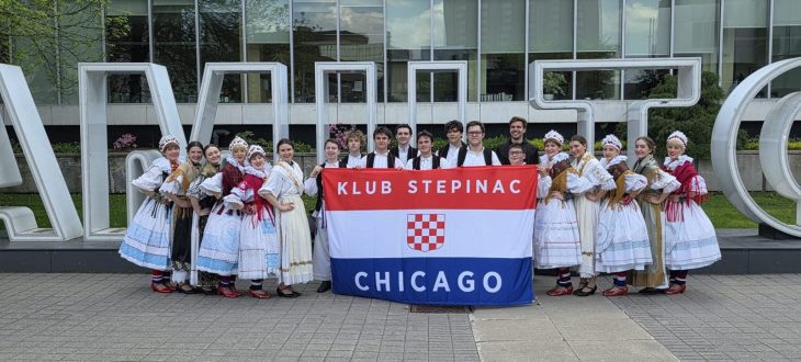 Klub Stepinac dancers in Croatian folk costumes holding the Klub Stepinac Chicago flag in front of the HAMILTON sign at Hamilton City Hall.