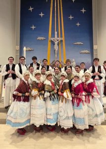 Klub Stepinac dancers in folk costumes posing for a group photo in front of the altar of a church in Hamilton.