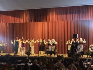 Klub Stepinac performing on stage in Dalmatian folk costumes, with tamburaši playing at the side.